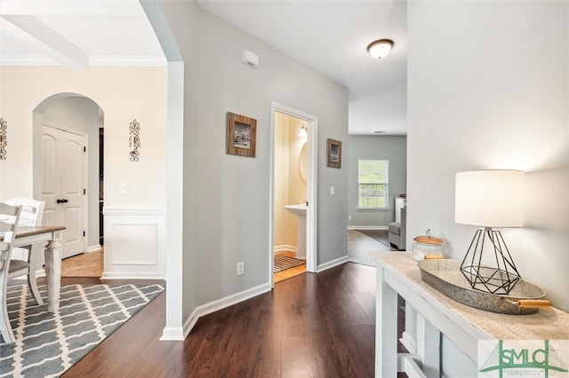 corridor with arched walkways, baseboards, crown molding, and dark wood finished floors