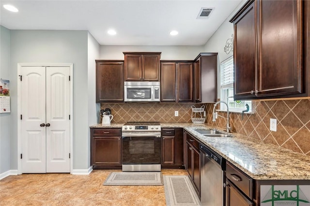 kitchen featuring dark brown cabinets, light stone countertops, visible vents, appliances with stainless steel finishes, and a sink