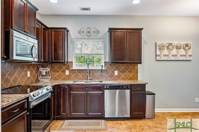 kitchen with visible vents, a sink, dark brown cabinets, stainless steel appliances, and light stone counters