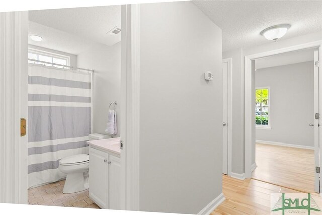 bathroom with a textured ceiling, vanity, visible vents, toilet, and wood finished floors