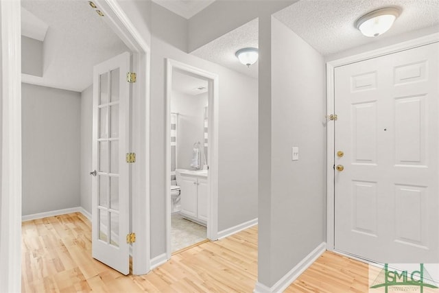 entryway with baseboards, light wood finished floors, and a textured ceiling