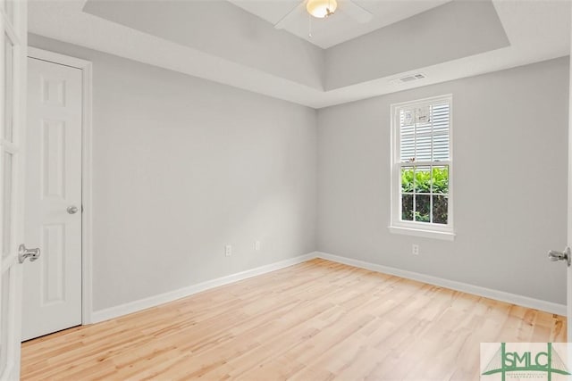 empty room with a tray ceiling, wood finished floors, baseboards, and visible vents