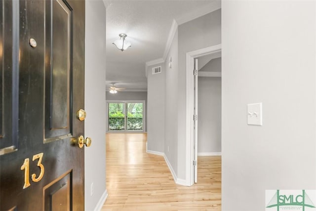 corridor featuring crown molding, visible vents, baseboards, and light wood-style floors