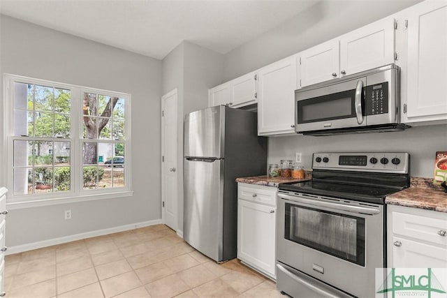 kitchen featuring dark stone countertops, light tile patterned floors, white cabinets, baseboards, and stainless steel appliances