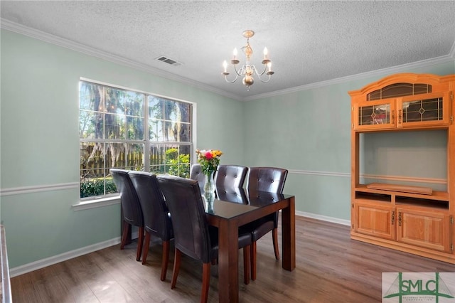 dining space with a notable chandelier, a textured ceiling, crown molding, visible vents, and wood finished floors
