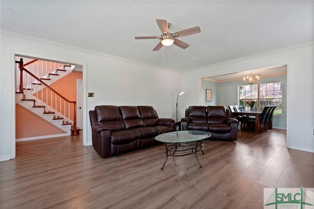 living area with crown molding, ceiling fan with notable chandelier, wood finished floors, stairs, and baseboards