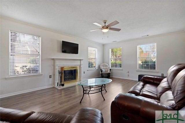 living area with wood finished floors, a fireplace with flush hearth, crown molding, and ceiling fan
