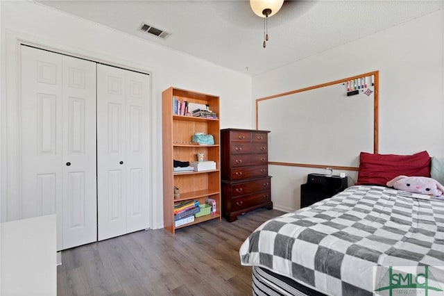 bedroom with dark wood-style flooring, visible vents, ceiling fan, and a closet