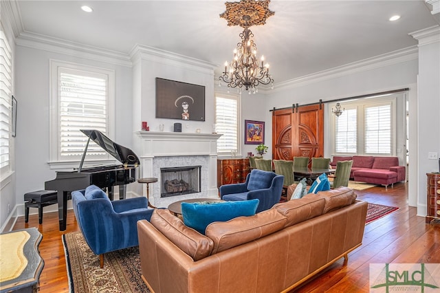 living area with an inviting chandelier, a barn door, hardwood / wood-style flooring, crown molding, and a premium fireplace