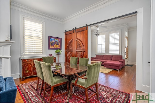 dining room with baseboards, ornamental molding, a barn door, and hardwood / wood-style flooring