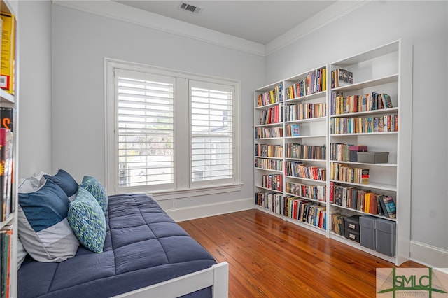 living area with visible vents, baseboards, built in shelves, ornamental molding, and wood finished floors