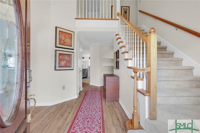 foyer featuring stairway, a towering ceiling, baseboards, and wood finished floors