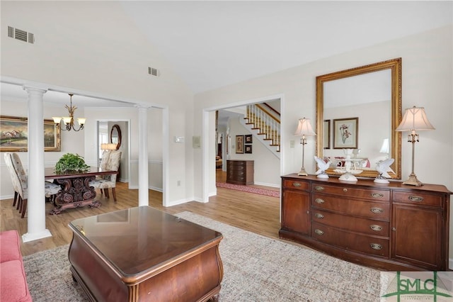 living area featuring visible vents, light wood-type flooring, decorative columns, a chandelier, and stairs