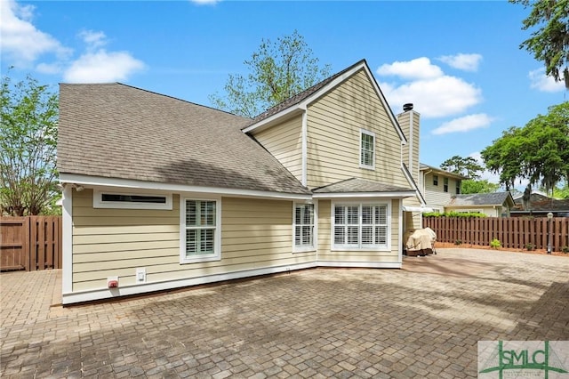 rear view of property featuring roof with shingles, a chimney, a patio area, and fence