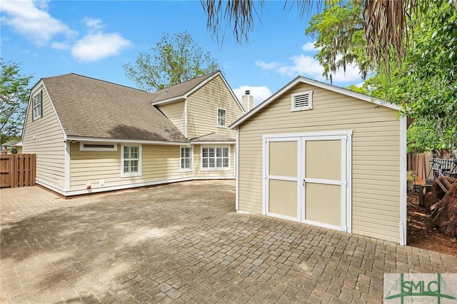 back of property featuring roof with shingles, a patio area, a storage shed, an outbuilding, and fence