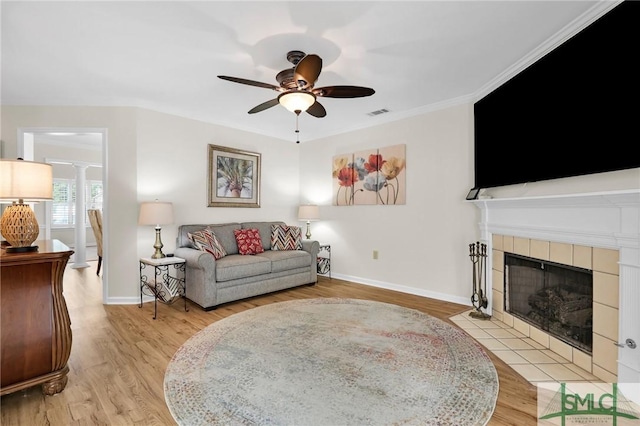 living room featuring baseboards, a tiled fireplace, ornamental molding, ceiling fan, and wood finished floors