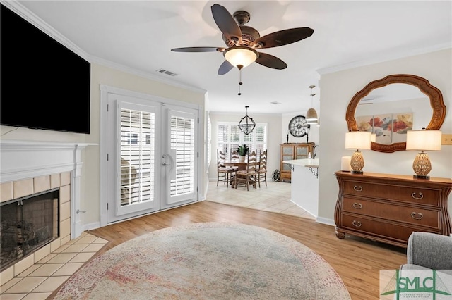 living room featuring a tiled fireplace, ornamental molding, light wood-style floors, and visible vents
