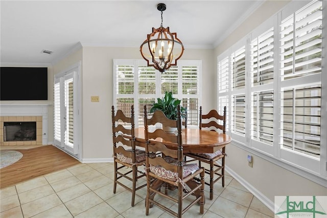 dining space featuring light tile patterned floors, an inviting chandelier, ornamental molding, a tile fireplace, and baseboards