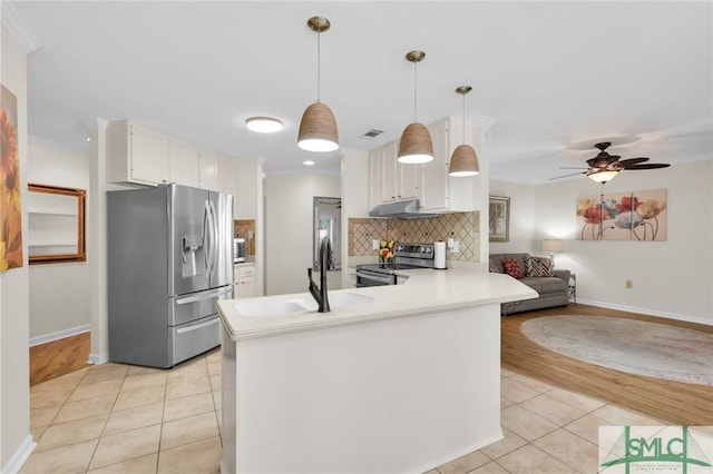 kitchen featuring light tile patterned floors, a peninsula, under cabinet range hood, stainless steel appliances, and decorative backsplash