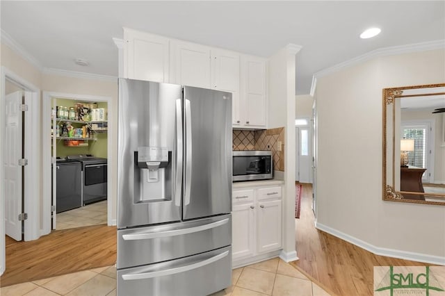 kitchen with white cabinetry, crown molding, light tile patterned flooring, stainless steel appliances, and washing machine and clothes dryer