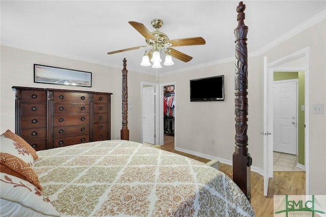 bedroom featuring a closet, ornamental molding, a spacious closet, light wood finished floors, and baseboards