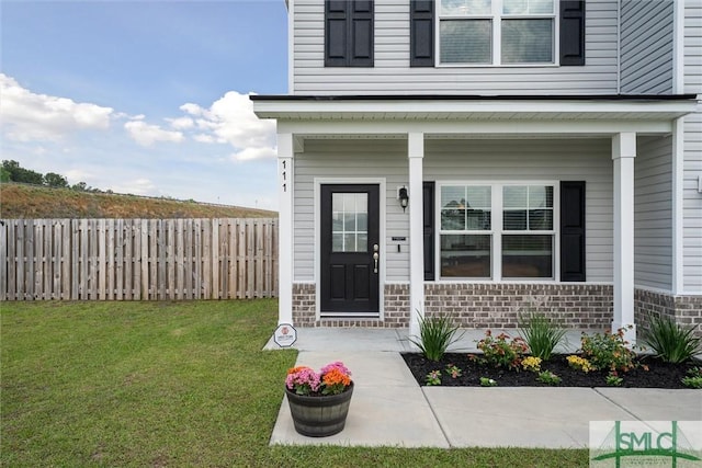 view of exterior entry featuring covered porch, a lawn, stone siding, fence, and brick siding