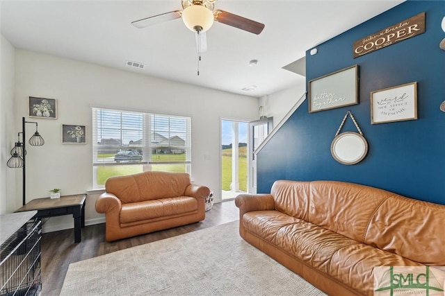 living area with ceiling fan, an accent wall, visible vents, wood finished floors, and baseboards