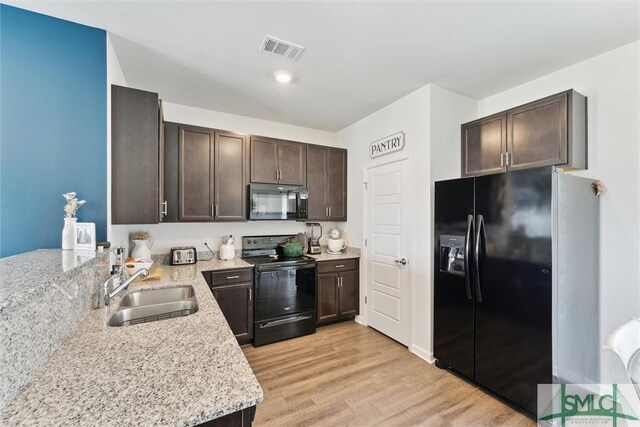 kitchen featuring visible vents, a sink, dark brown cabinets, black appliances, and light wood-style flooring