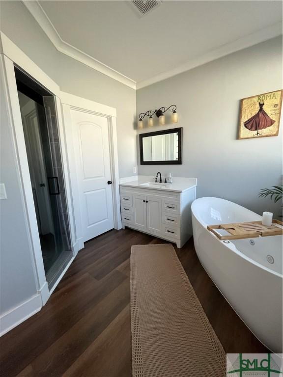 bathroom with vanity, a freestanding tub, wood finished floors, visible vents, and ornamental molding