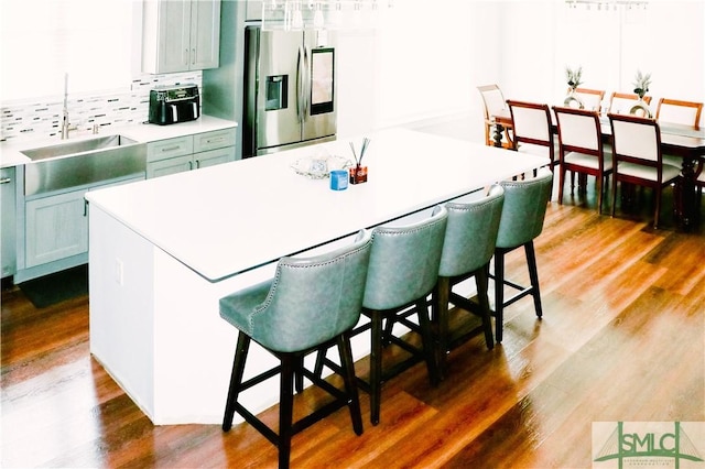 kitchen with stainless steel refrigerator with ice dispenser, light countertops, a kitchen breakfast bar, and a center island
