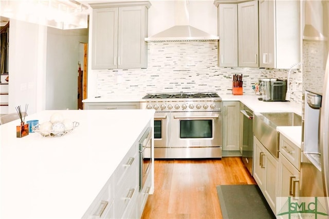 kitchen featuring wall chimney range hood, light countertops, tasteful backsplash, light wood finished floors, and stainless steel appliances