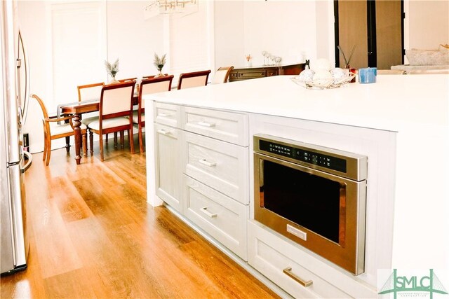 kitchen featuring light wood-type flooring, freestanding refrigerator, white cabinetry, and light countertops