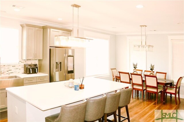 kitchen featuring light countertops, ornamental molding, stainless steel fridge with ice dispenser, and a breakfast bar area