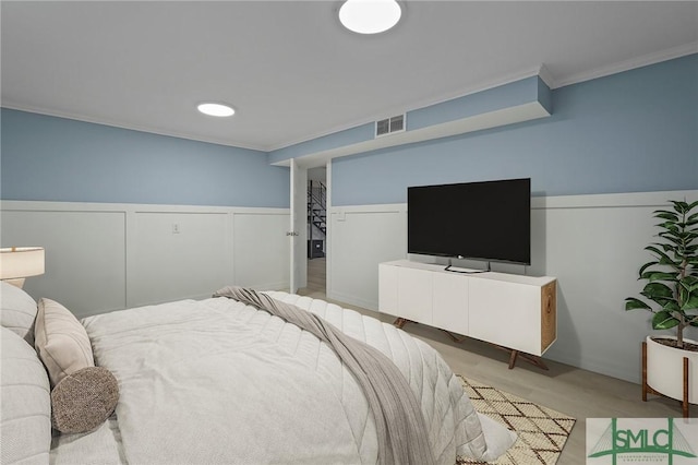bedroom with ornamental molding, a wainscoted wall, visible vents, and light wood-style flooring