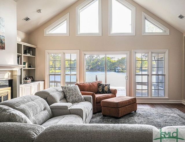 living area featuring wood finished floors, high vaulted ceiling, visible vents, and a water view