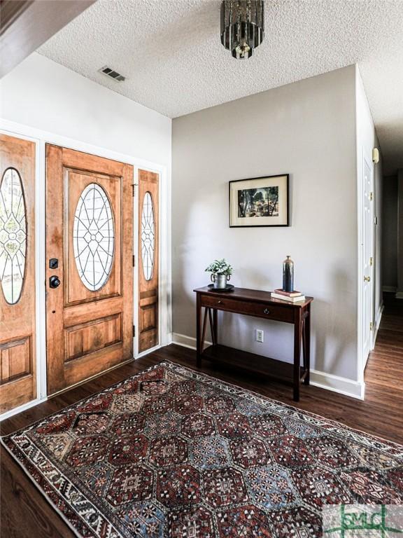 foyer entrance featuring a textured ceiling, baseboards, dark wood finished floors, and visible vents
