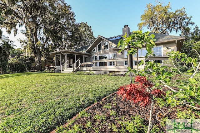 back of property with a sunroom, a lawn, and a chimney