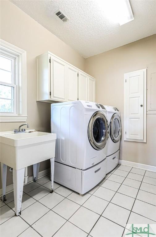 laundry area with light tile patterned floors, a textured ceiling, visible vents, washing machine and clothes dryer, and cabinet space