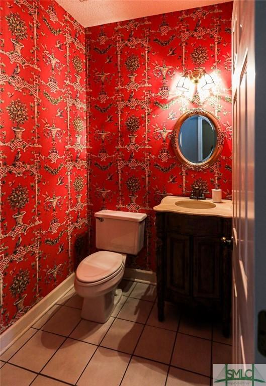half bath with tile patterned flooring, toilet, vanity, and baseboards