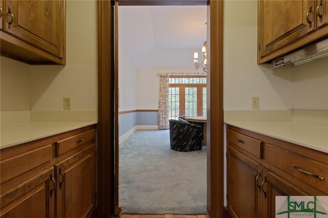 kitchen featuring light countertops, a notable chandelier, carpet, and brown cabinetry