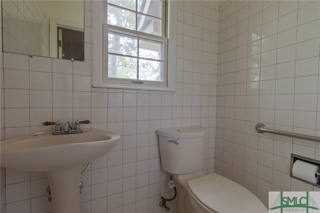 bathroom with tile walls, a sink, and toilet