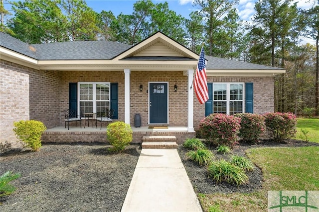 view of front of property featuring brick siding, a shingled roof, and covered porch