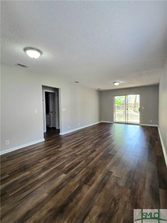 empty room featuring visible vents, a textured ceiling, baseboards, and dark wood-style floors