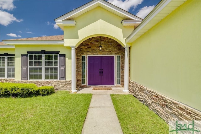entrance to property featuring stucco siding, stone siding, and a lawn