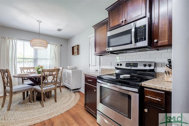 kitchen featuring tasteful backsplash, dark brown cabinets, light wood-style floors, stainless steel appliances, and hanging light fixtures