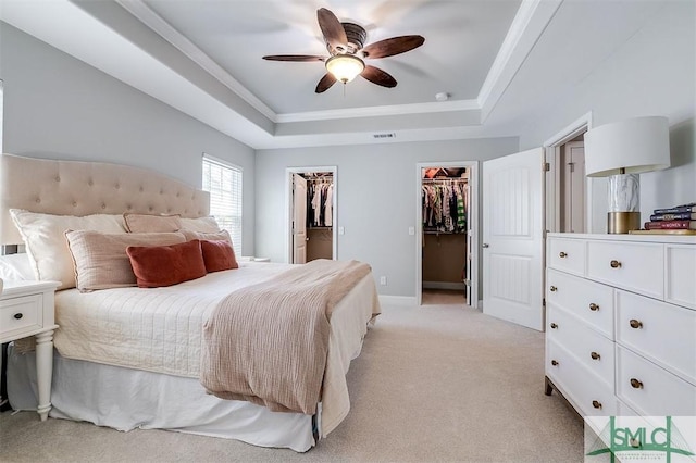 bedroom featuring ceiling fan, light colored carpet, ornamental molding, a spacious closet, and a raised ceiling
