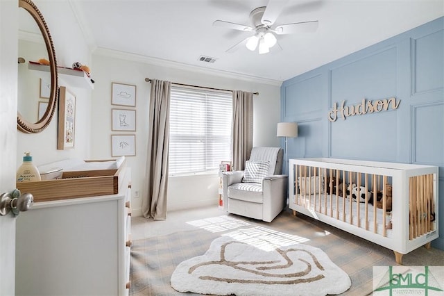 bedroom with visible vents, a nursery area, ceiling fan, carpet, and crown molding