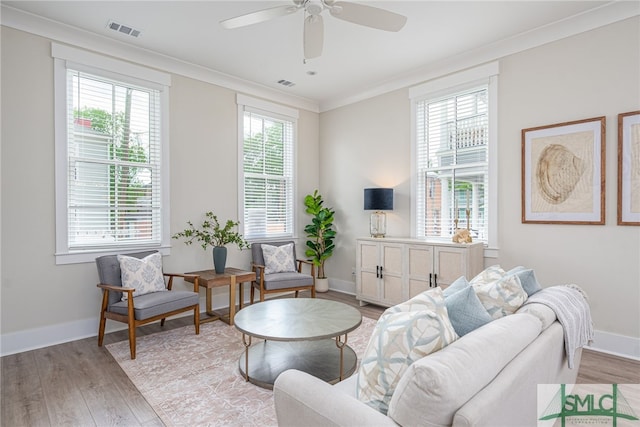 living room with a ceiling fan, ornamental molding, visible vents, light wood finished floors, and baseboards