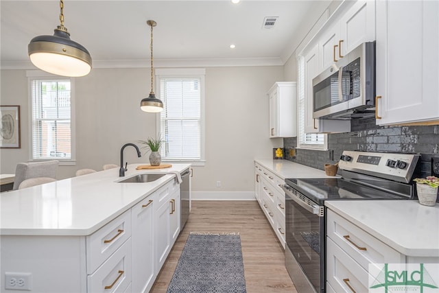 kitchen featuring ornamental molding, light wood-style flooring, a kitchen island with sink, appliances with stainless steel finishes, and a sink