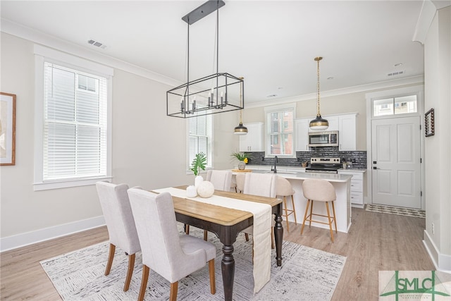 dining room with crown molding, visible vents, a notable chandelier, and light wood-style floors